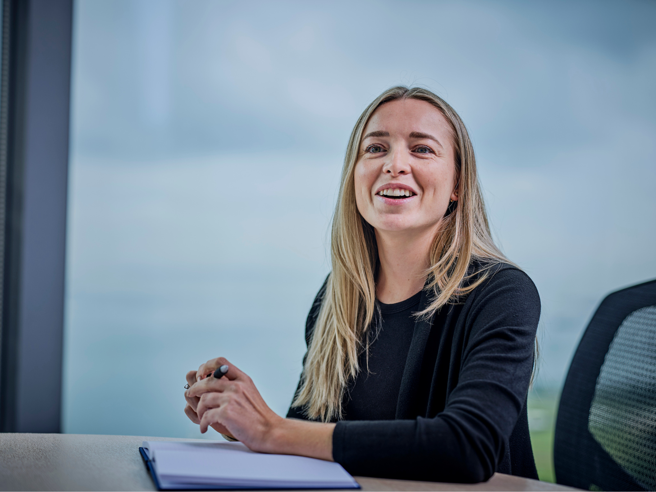 woman sitting at table with notepad and pen, smiling