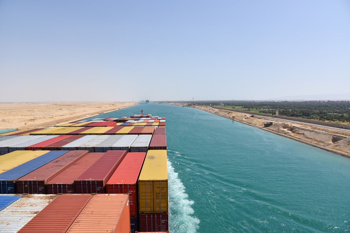 Container ship navigating a canal under clear skies.