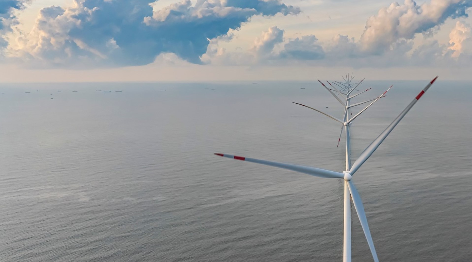 Aerial view of an offshore wind turbine with boats visible on the horizon.