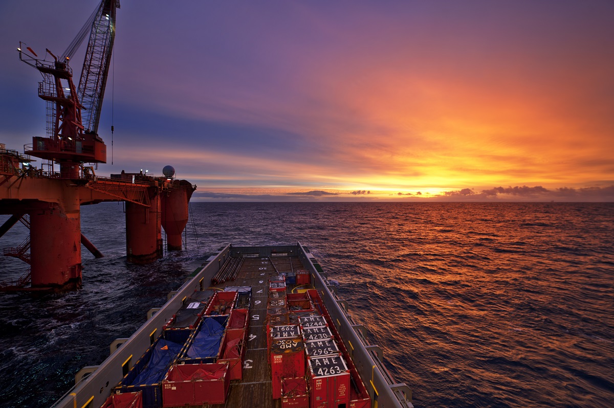 Oil rig at sunset over calm ocean waters.