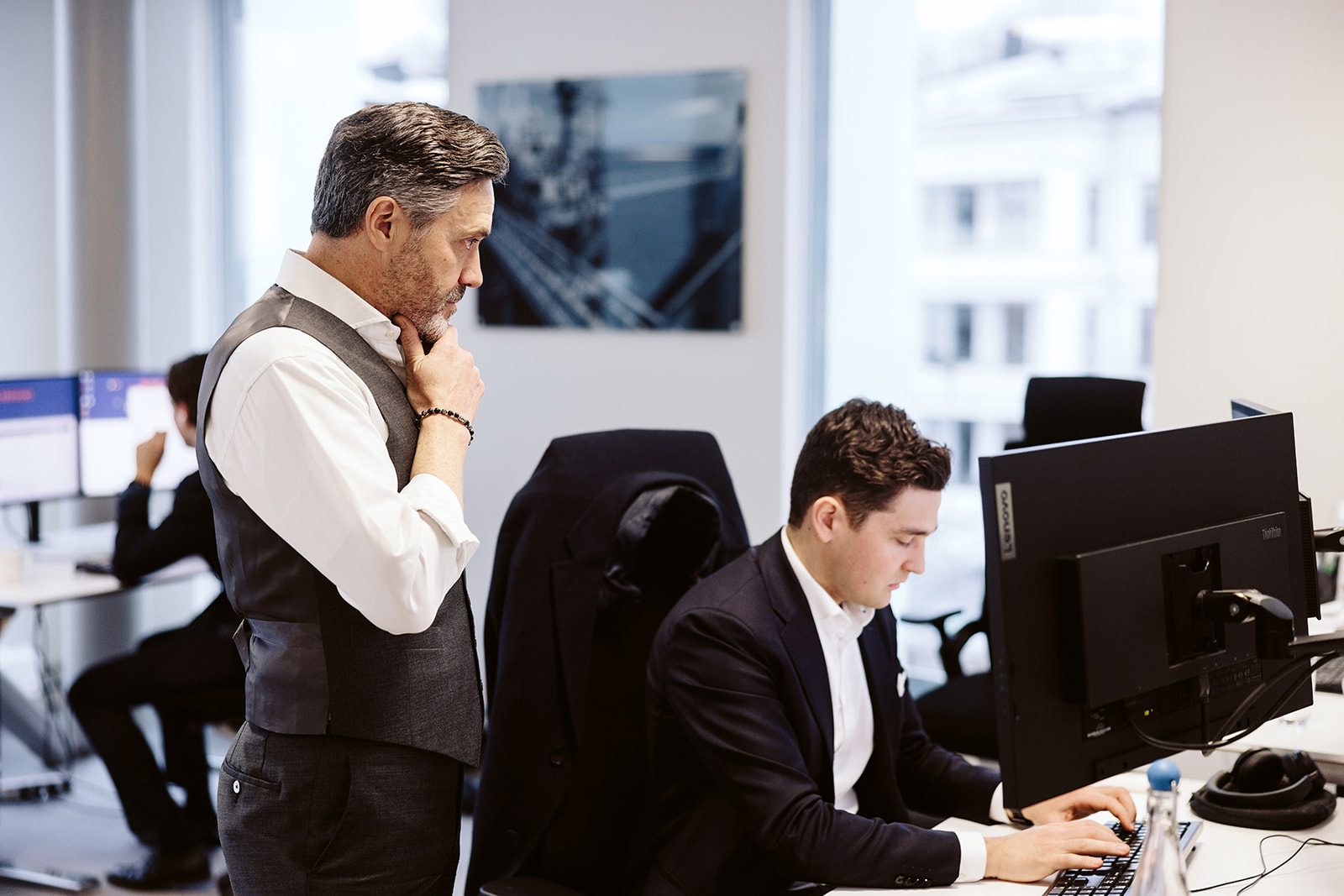 Two men in an office setting, one observing.