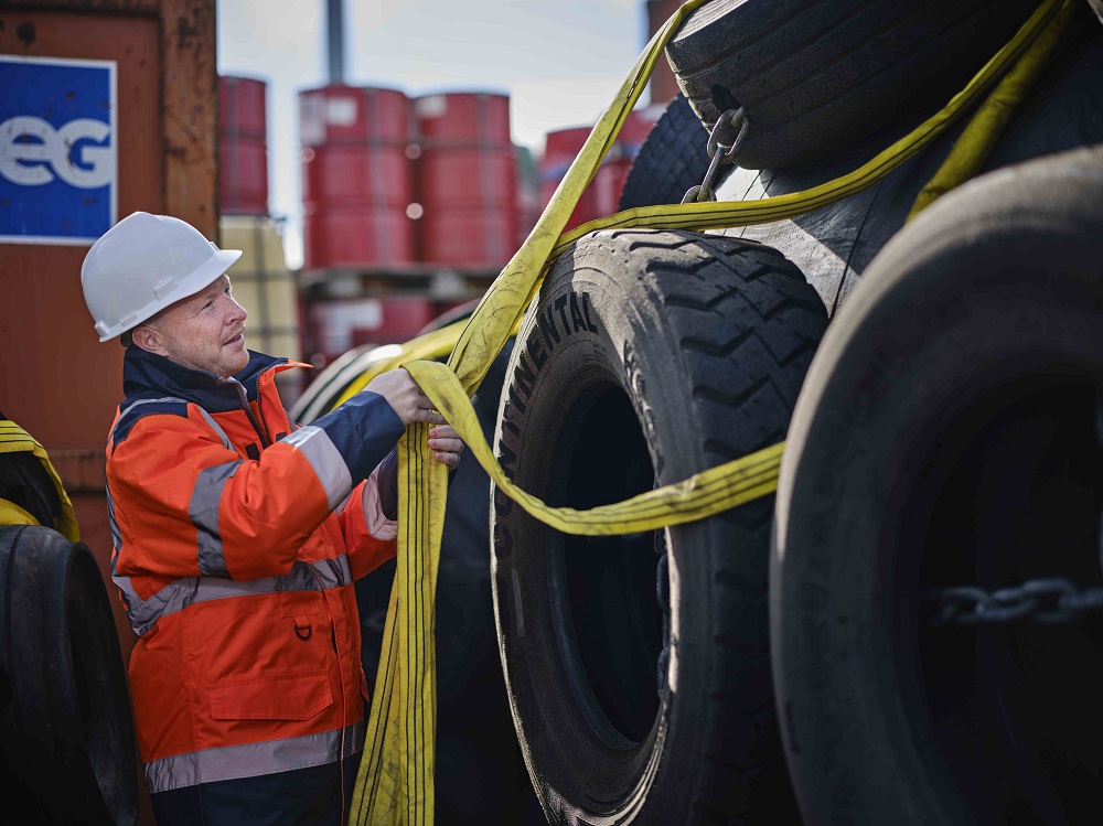 Worker securing tires with straps in storage.