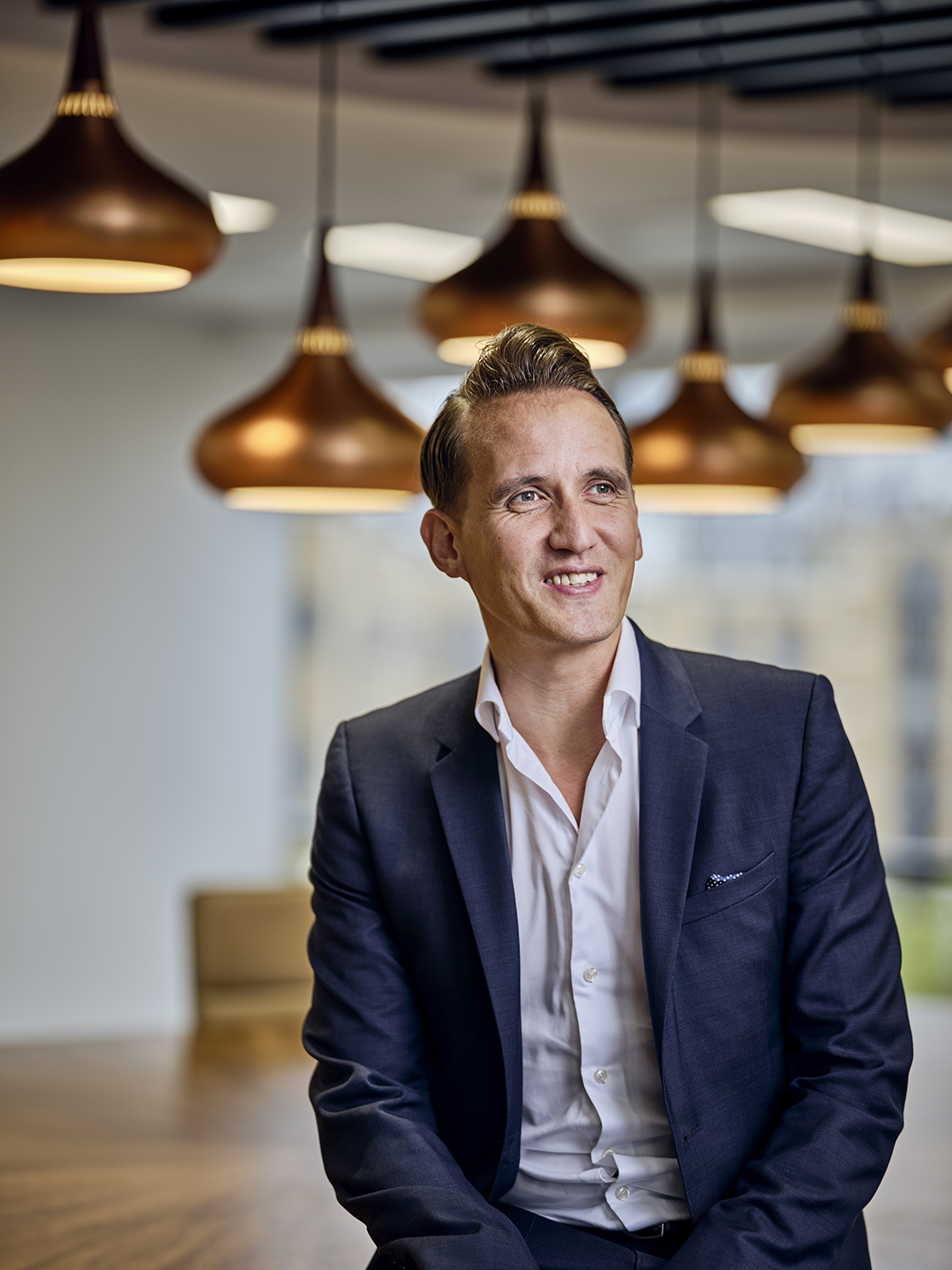 Man in a suit sitting under pendant lights.
