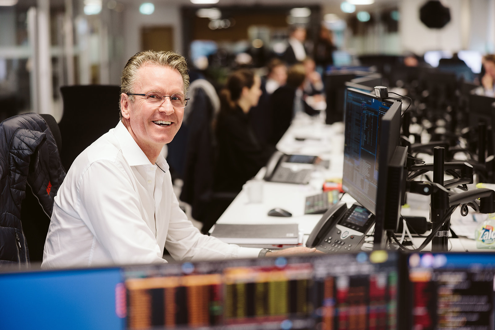 Smiling man at a desk with computer screens.
