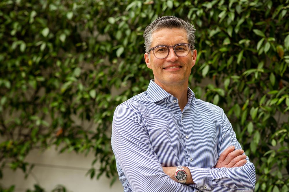 Man smiling with arms crossed, green background.