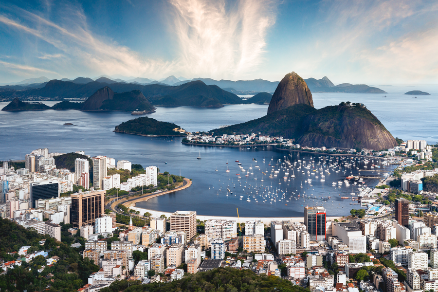 Panoramic view of a coastal city with a waterfront, mixed architecture, and boats on calm water.