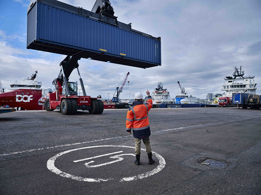 Worker signals as a container is lifted at port.