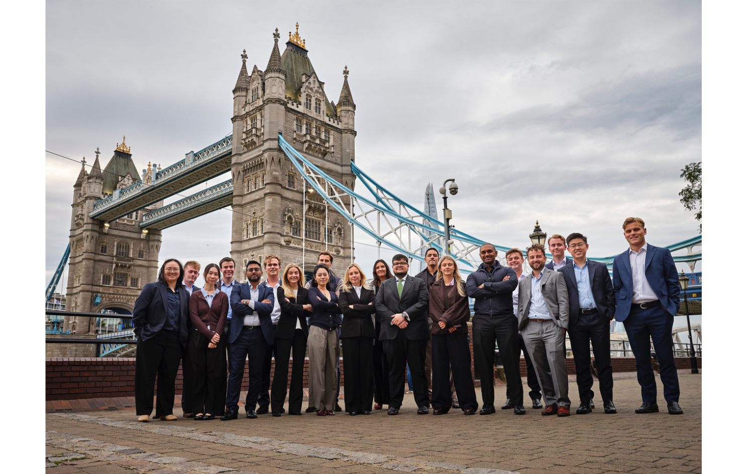 Diverse group of people in business and casual attire standing in front of London's Tower Bridge.