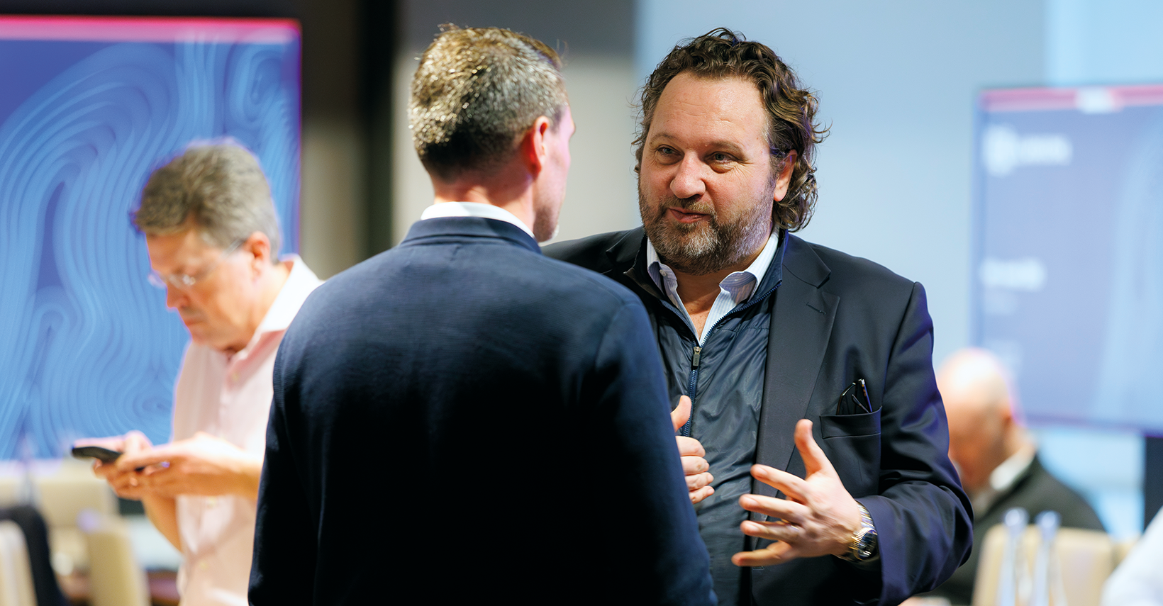 Two men in conversation, one in a dark sweater, one in a blazer.