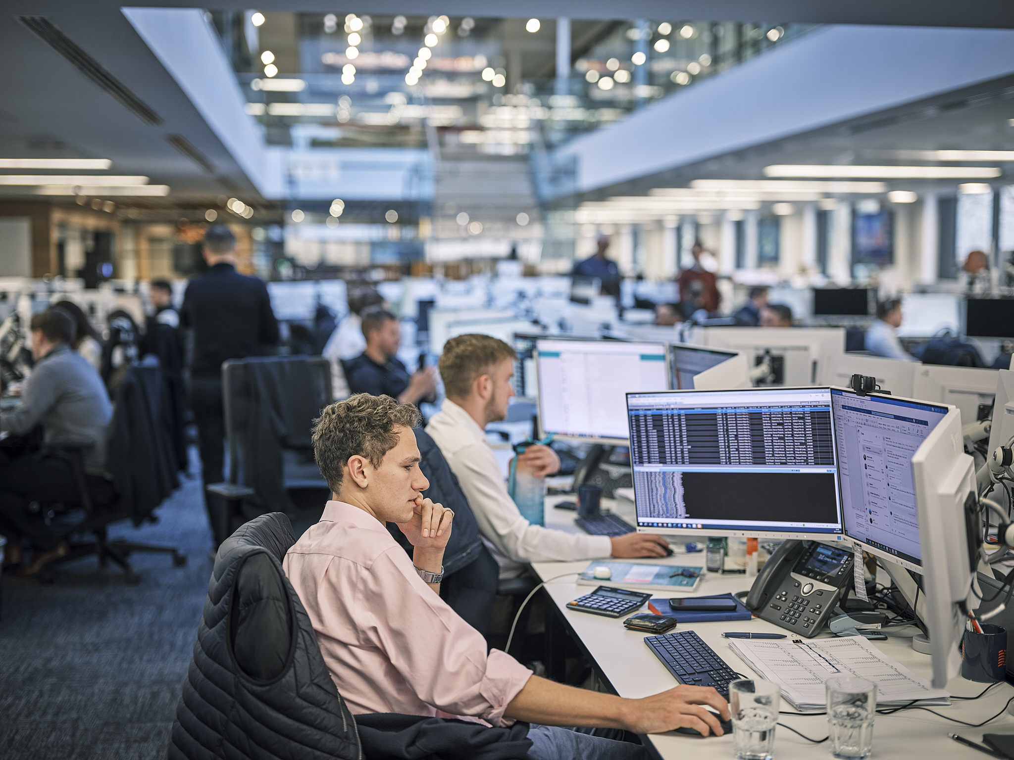 Office workers at computers in a busy workspace.