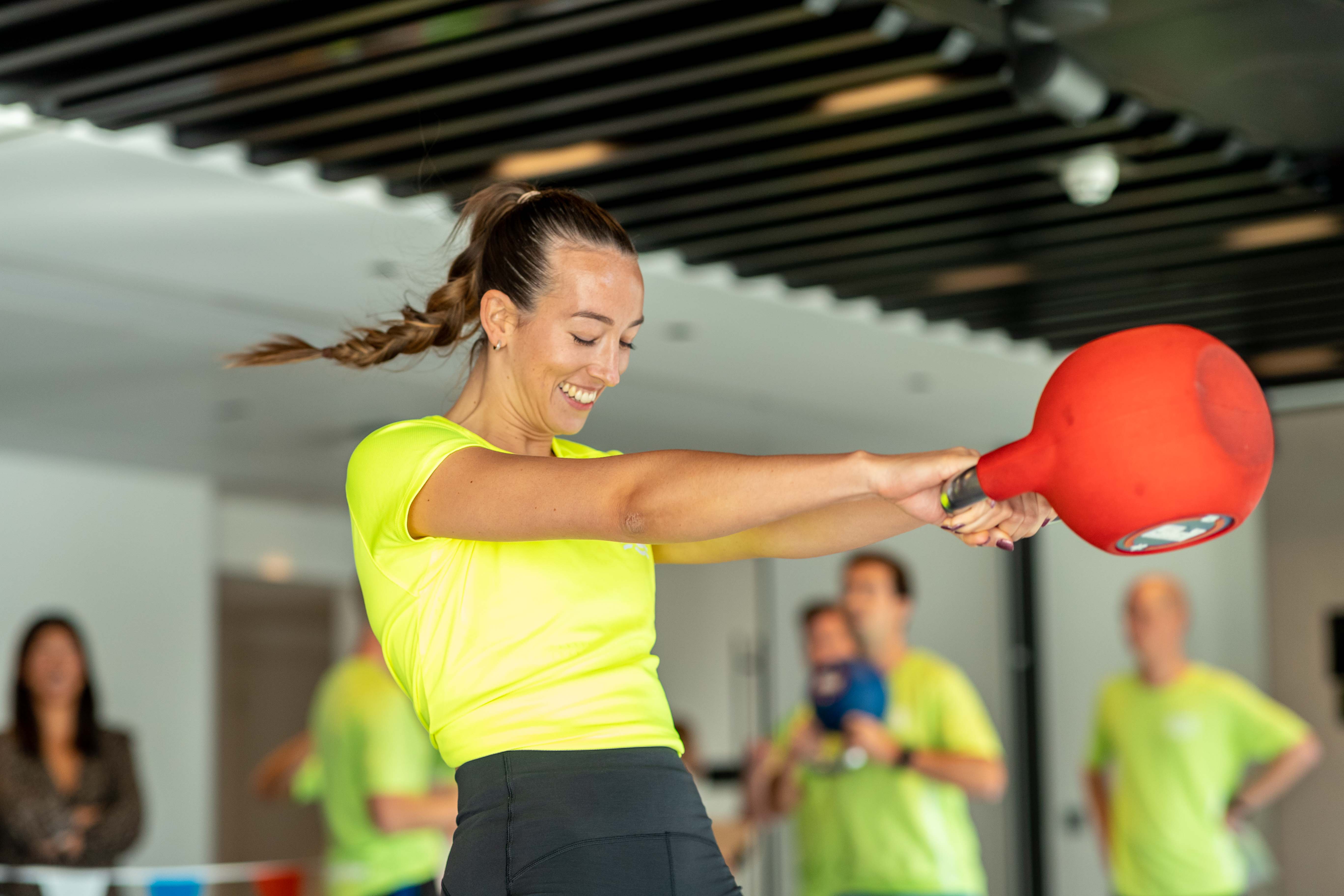 Woman in neon shirt swinging a kettlebell.