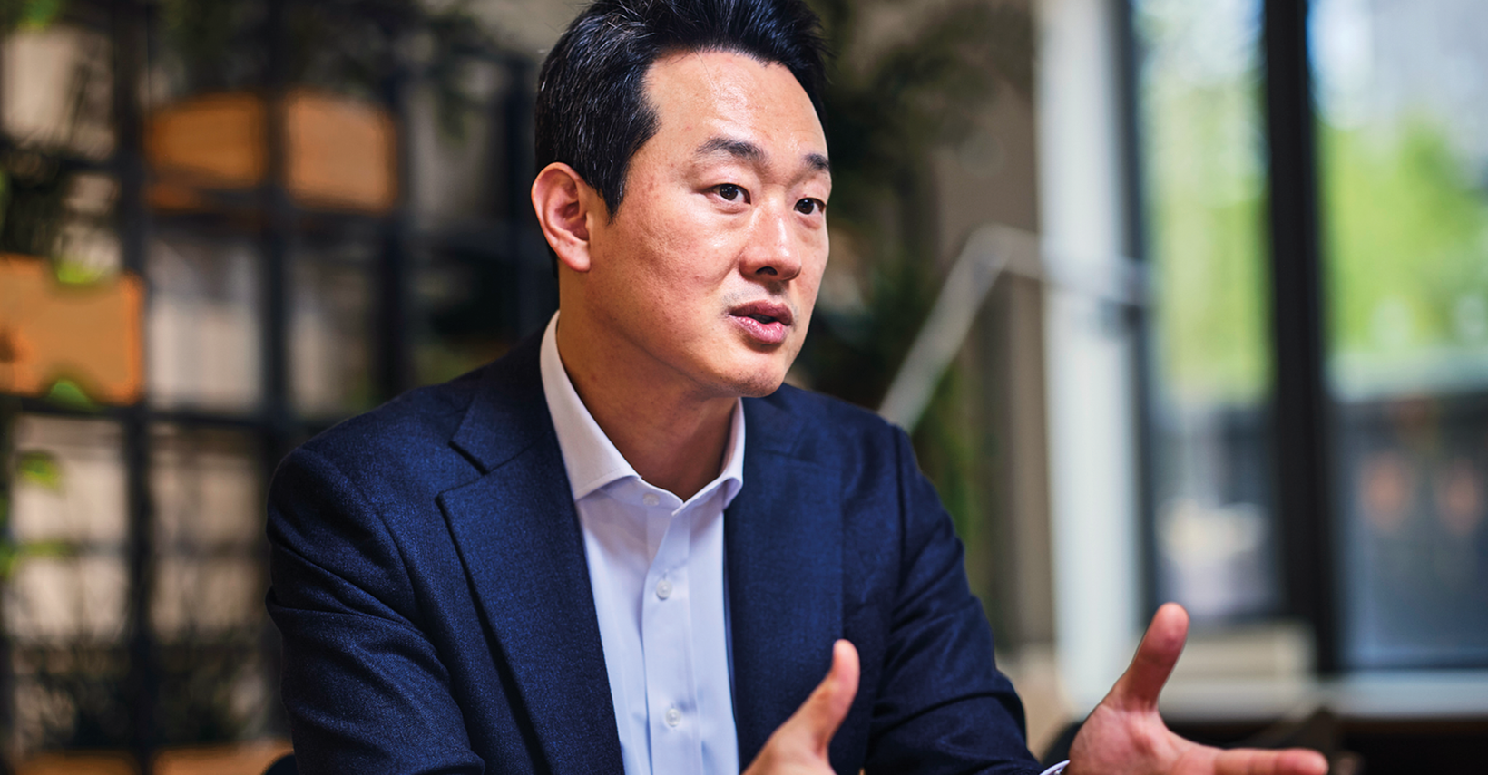 Man in a dark blazer engaged in conversation, gesturing with his hands.