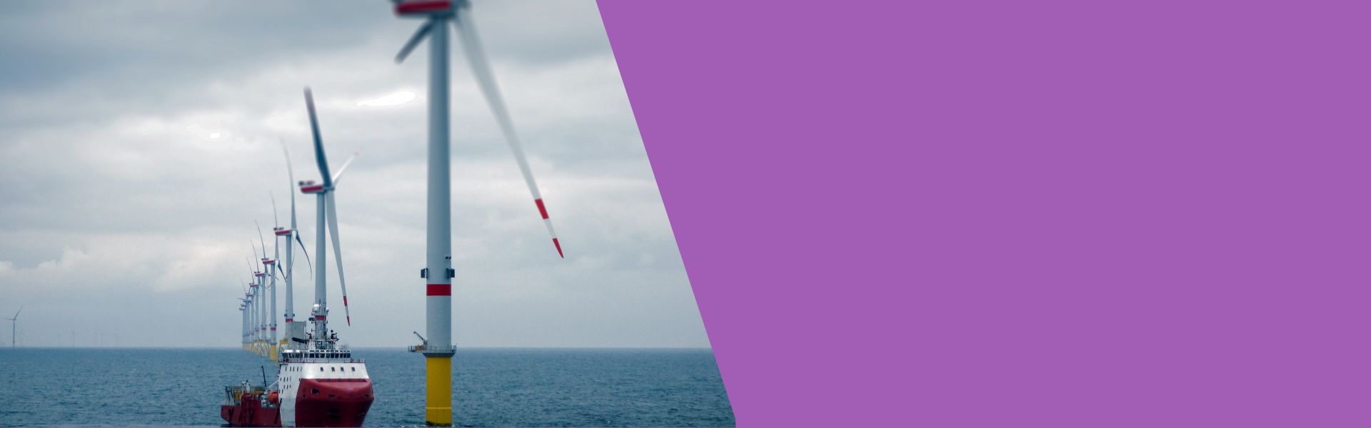 Row of wind turbines over the ocean, cloudy sky.