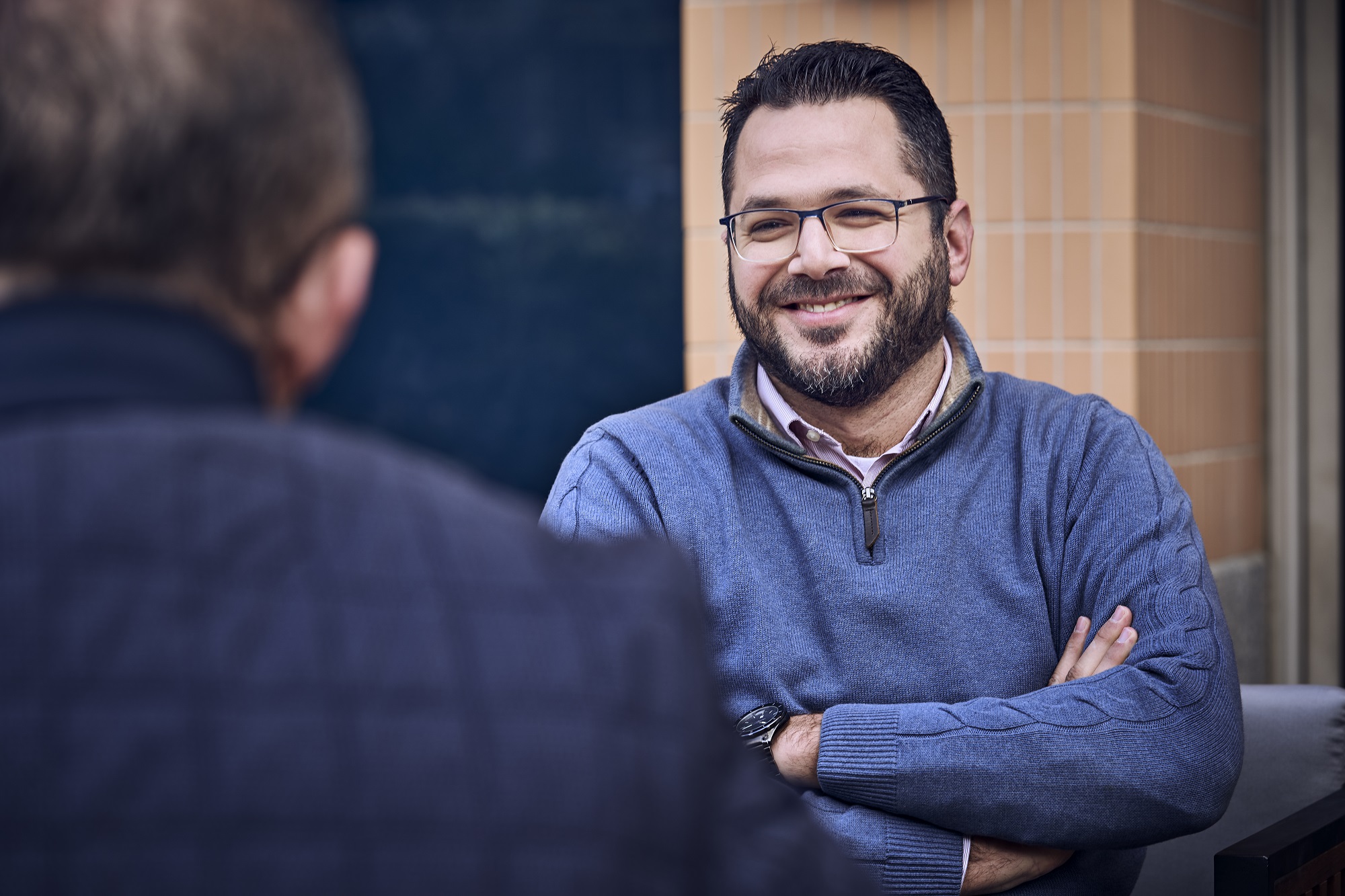 man with his arms crossed talking to colleague outside