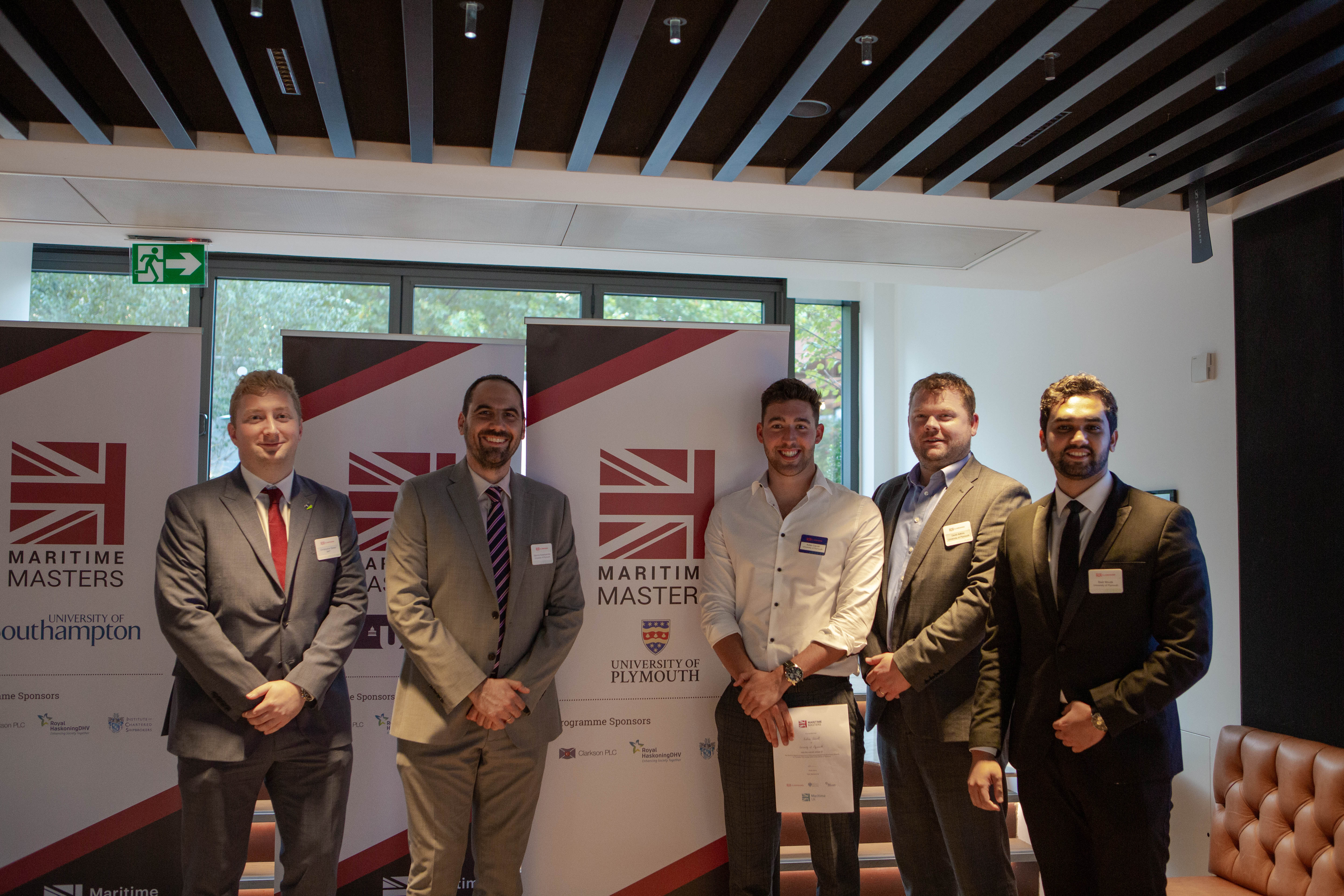 Five men in suits stand by Maritime Masters banners.