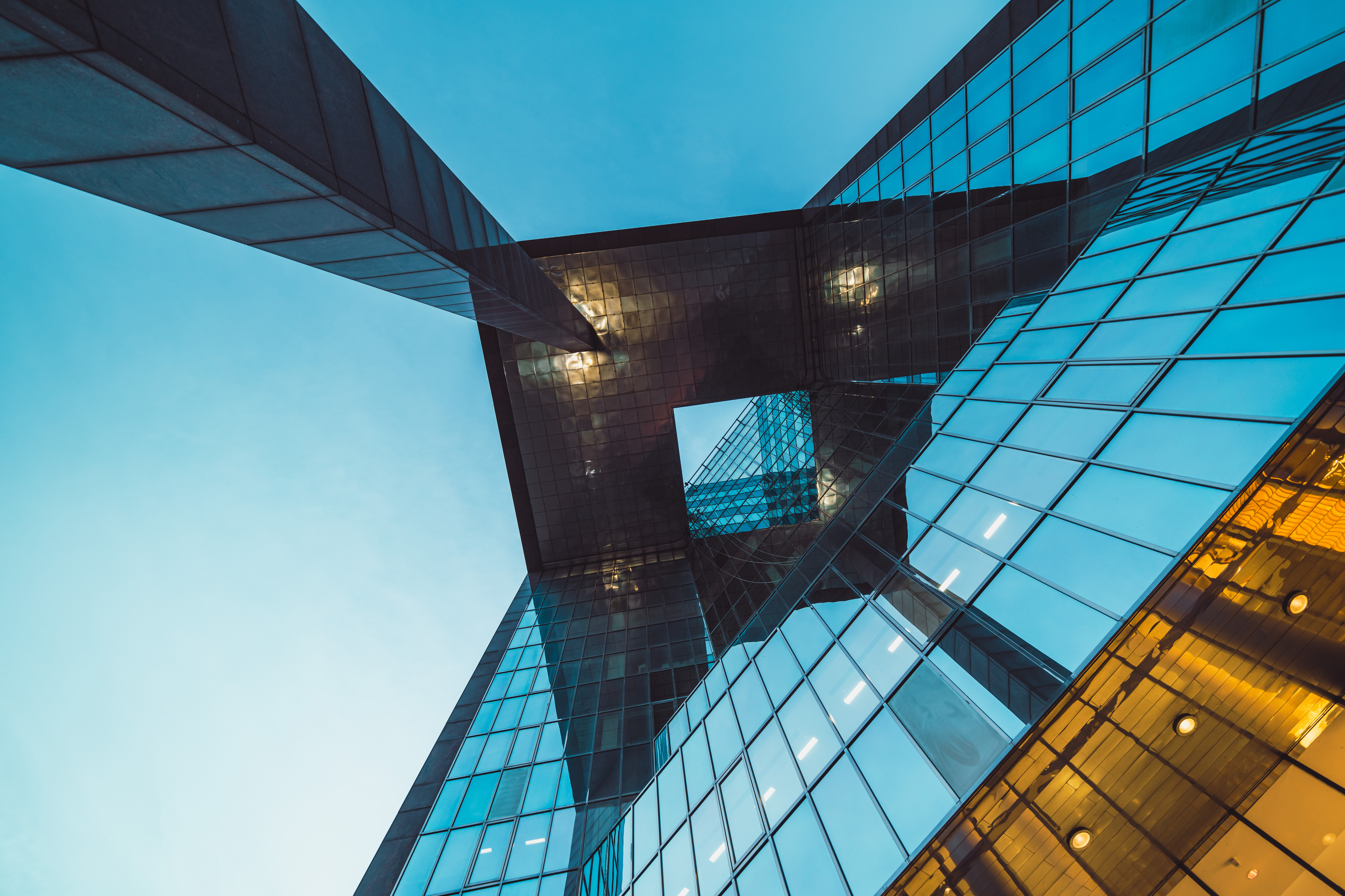 View looking upward at an angular, reflective modern building with glass and metal surfaces.